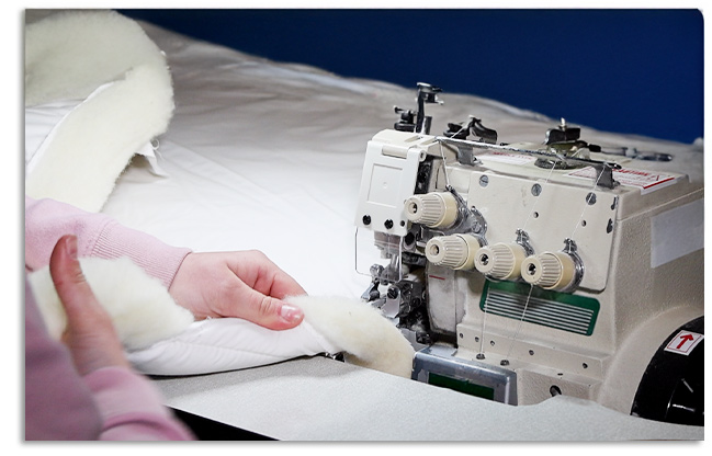 Close-up of a seamstress sewing a wool-filled duvet with an industrial sewing machine.